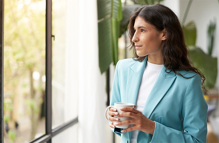 A woman stares peacefully out of the windows of her business, knowing the investment in window film is backed by 3M’s strong warranty.