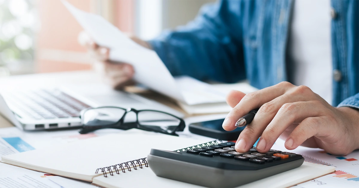 Hands hover over a calculator while holding papers as though paying bills; lower energy costs with 3M window film