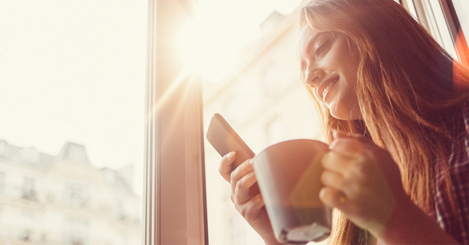 Woman looks at her phone next to window
