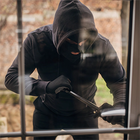 A man dressed in all black attempts to break into a glass door covered with 3M safety and security film.
